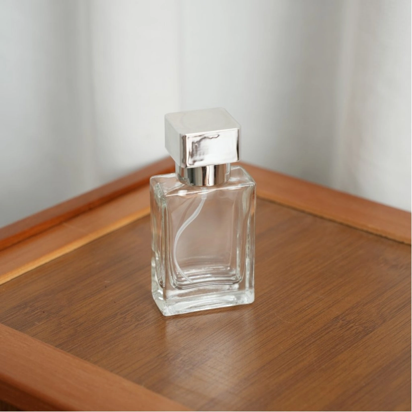 Clear square perfume bottle with a silver cap on a wooden table