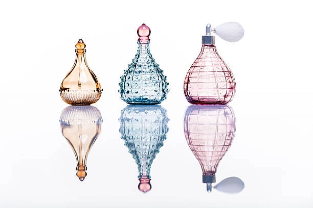 Three vintage-style glass perfume bottles with colorful tinted designs on a reflective surface