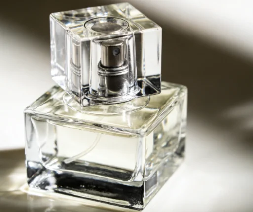 Close-up of a square clear glass perfume bottle with a thick base and silver pump.
